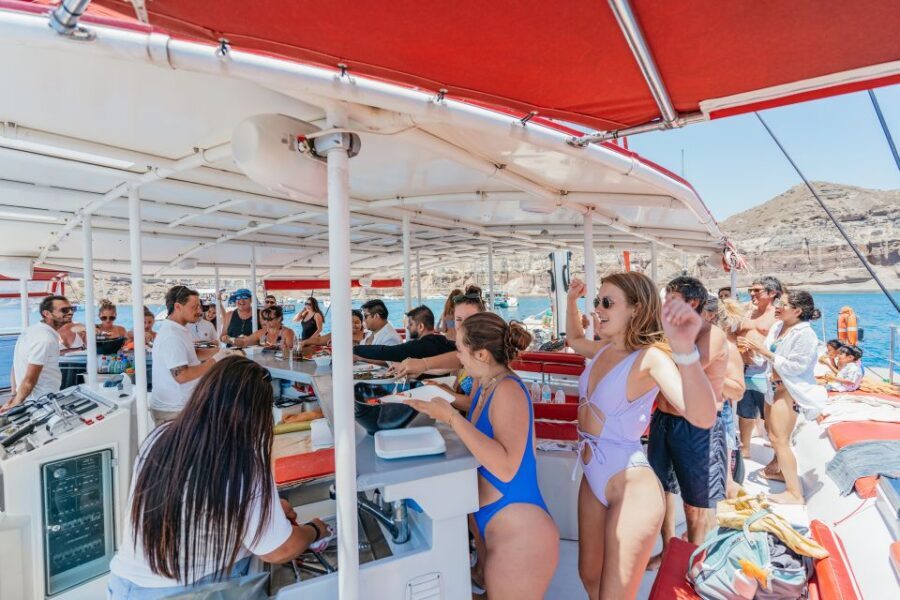 Santorini: Catamaran Tour with BBQ Dinner, Drinks, and Music - White Beach and its towering cliff shadows